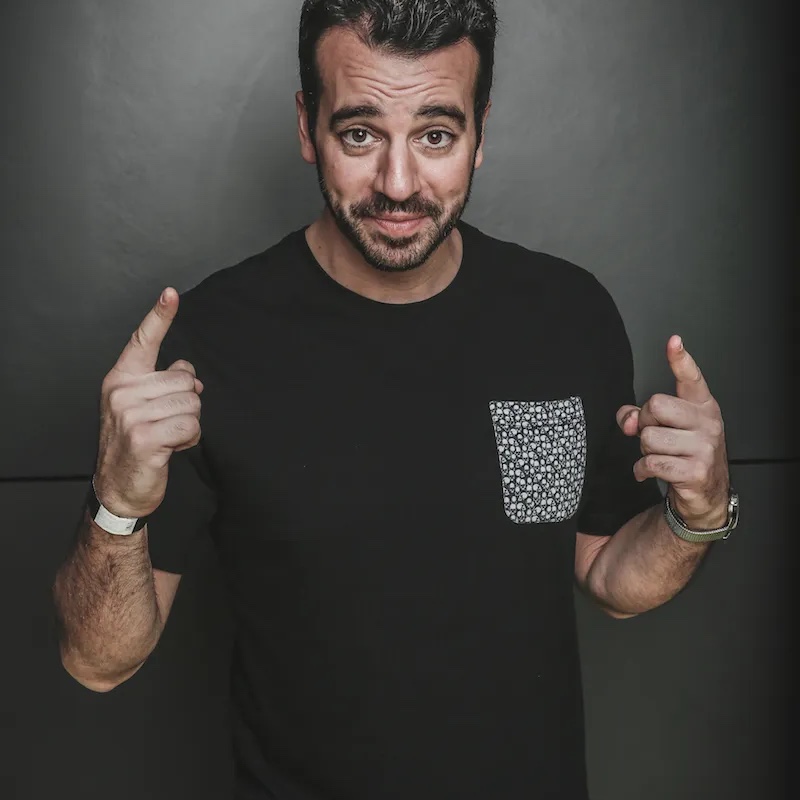 Steli Efti pointing upward against a dark background